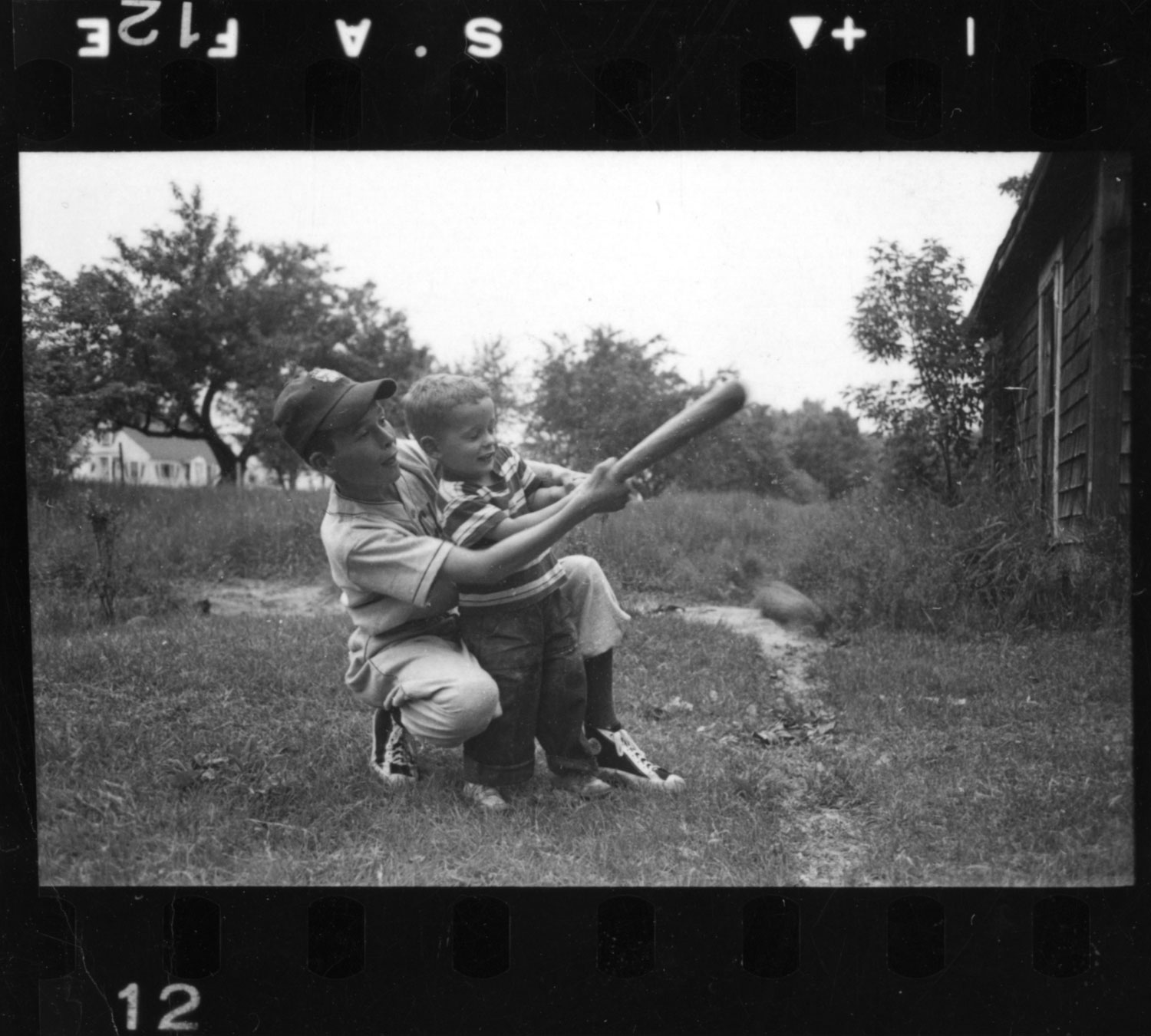 A Little Leaguer teaches a younger sibling how to bat, New Hampshire, 1954.