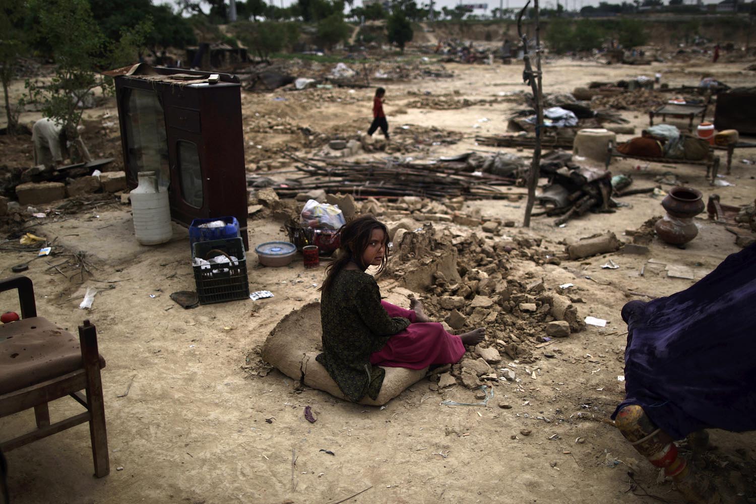 April 23, 2013. A Pakistani girl, who was displaced with her family by 2010 floods in Pakistan's Sindh province, sits next to her family's belongings among the rubble of her makeshift home, after it was destroyed, along with other homes, by the Capital Development Authority for being built on illegal lands, on the outskirts of Islamabad.
