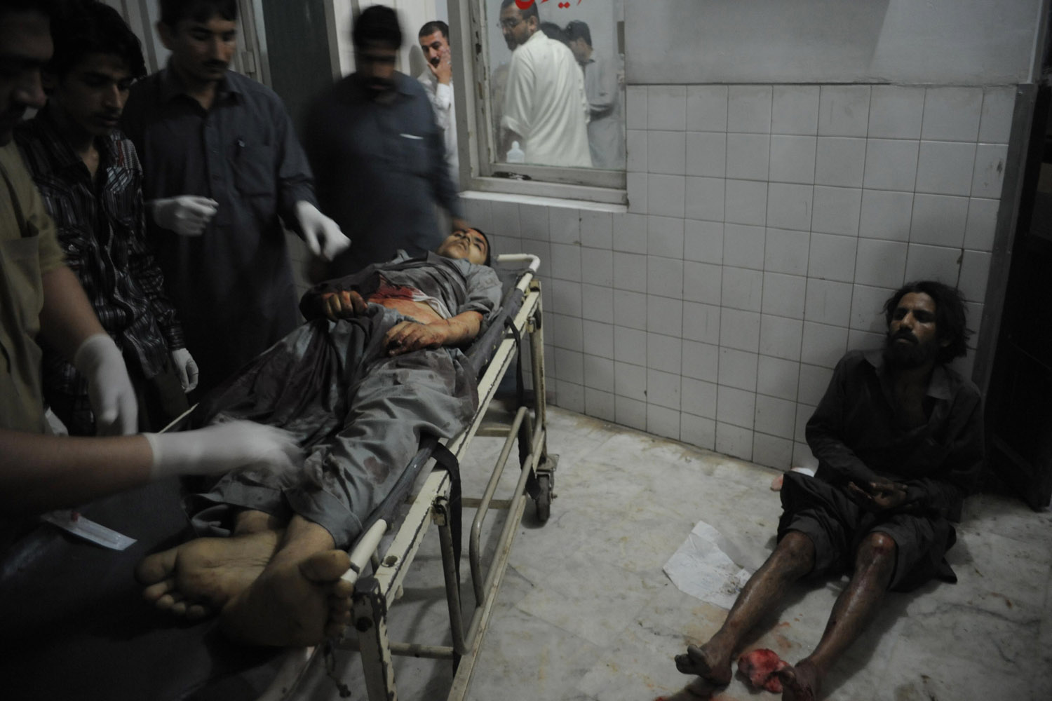 April 16, 2013. Pakistani paramedics treat an injured blast victim as an other victim waits for treatment at a hospital following a suicide bomb attack on a election campaign rally in Peshawar.
