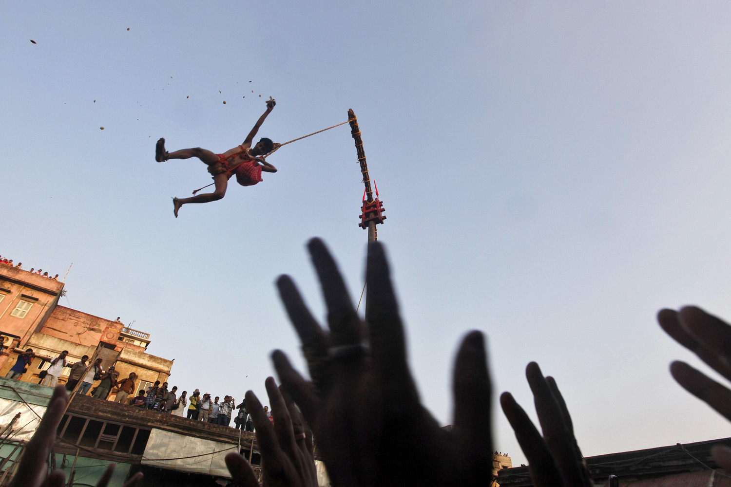 April 14, 2013. A Hindu devotee hanging from a rope throws offering towards other devotees during the  Chadak  ritual in Kolkata. Hundreds of Hindu devotees attend the ritual, held to worship the Hindu deity of destruction Lord Shiva, on the last day of the Bengali calendar year.