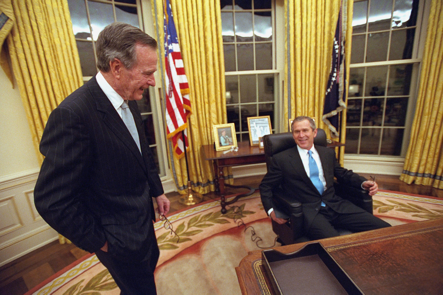 Jan. 20, 2001. George W. Bush, 43rd president of the United States, sits down at the Resolute desk in the Oval Office for the first time as his proud father, George H. W. Bush, the 41st president, looks on.