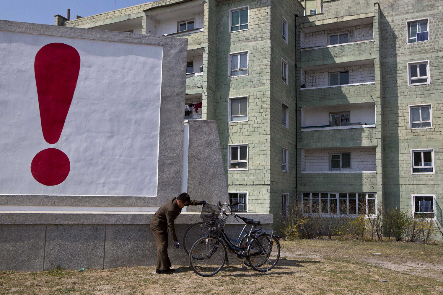 April 24, 2013. A North Korean man checks his bicycle next to a painted exclamation point on a propaganda billboard in Kaesong, North Korea.