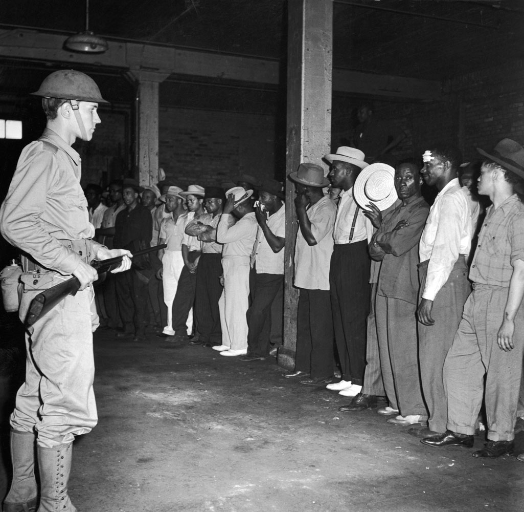 A soldier guards a group of African American men rounded up following wartime race riots in Detroit, 1943.