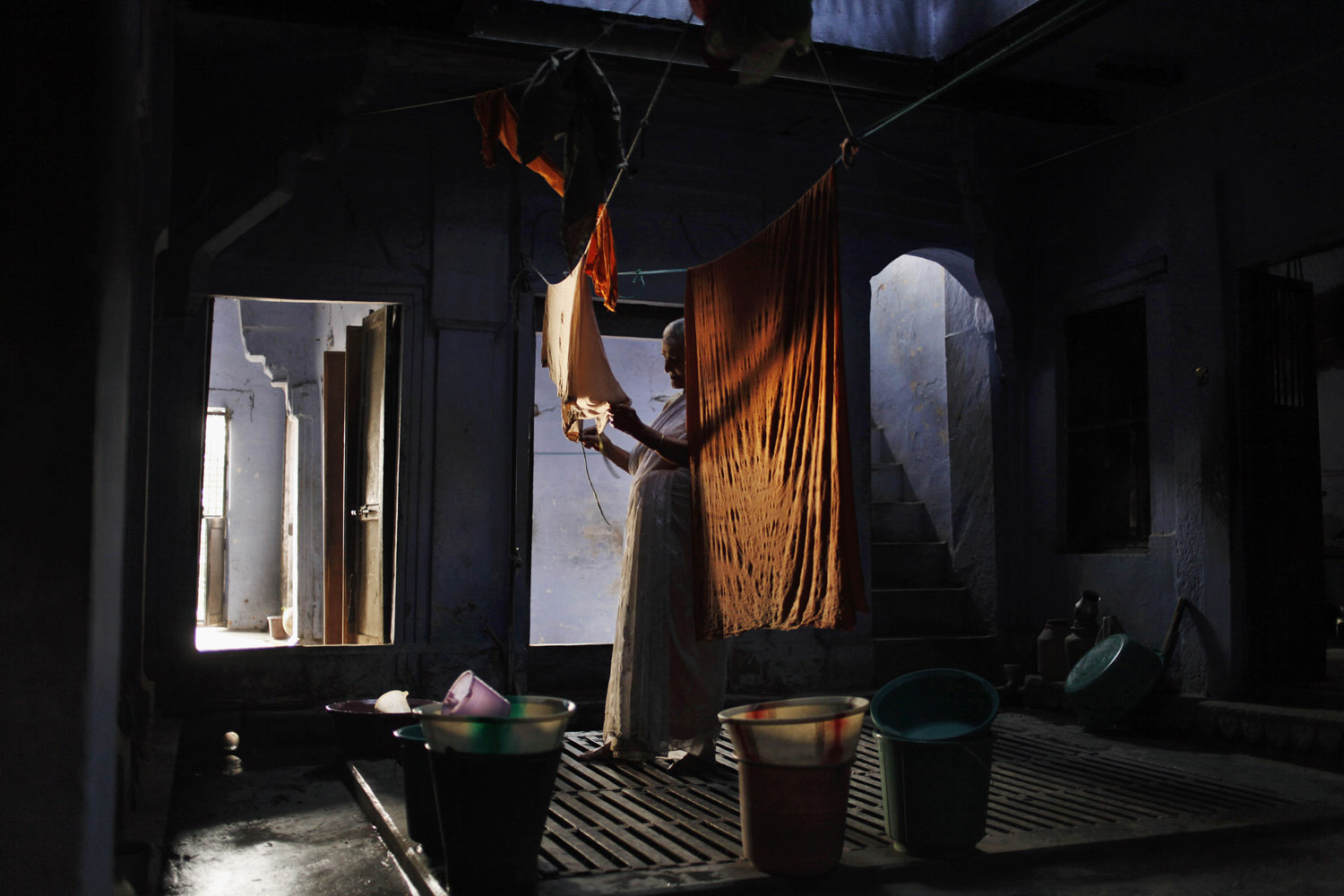 May 27, 2013. An elderly Indian widow hangs clothes to dry inside her small living quarter at an Ashram in Varanasi, India.