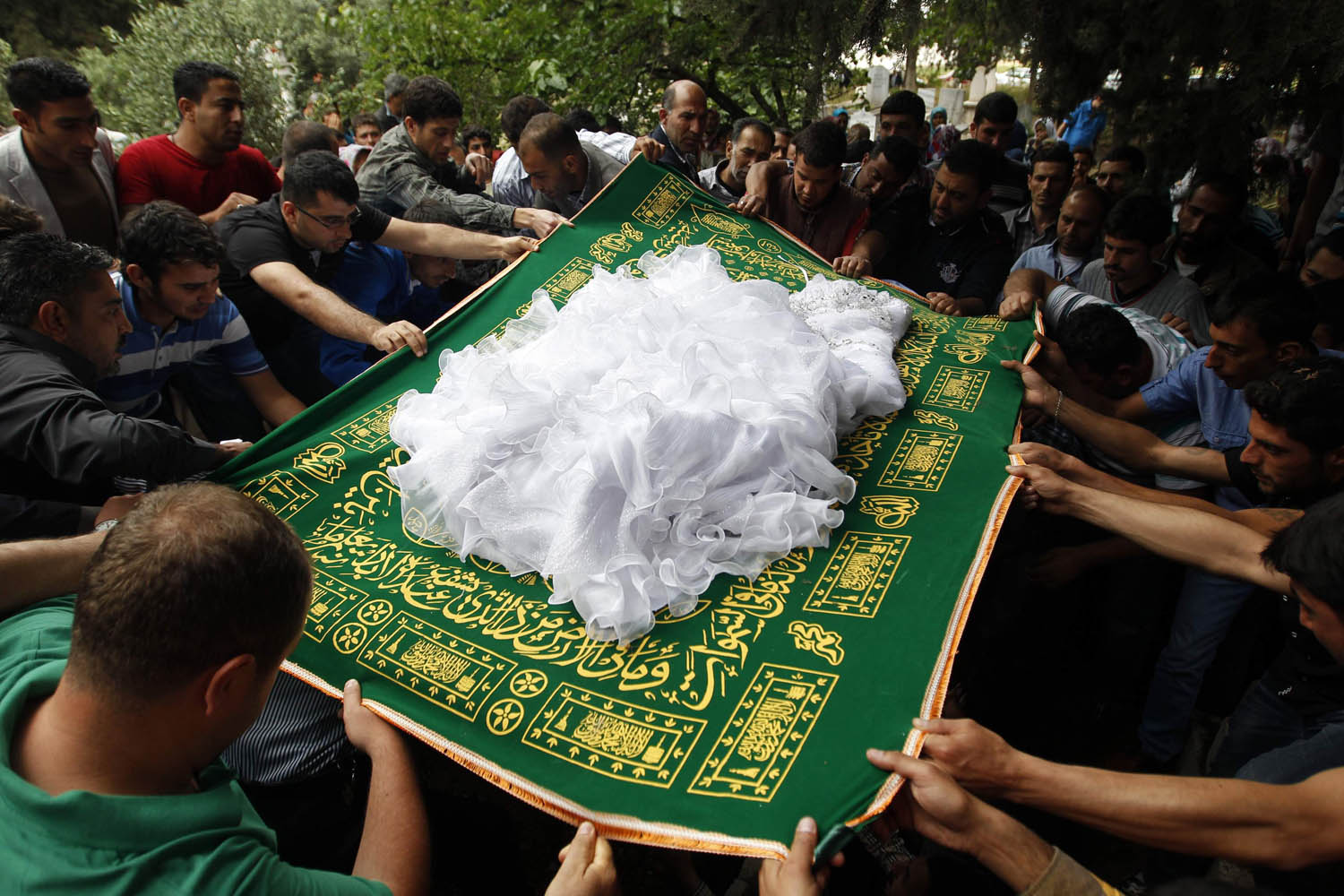 Relatives cover the body of 22-year-old Ayten Calim with a Muslim prayer rug and her wedding dress as they lower her into a grave in the town of Reyhanli in Hatay province near the Turkish-Syrian border