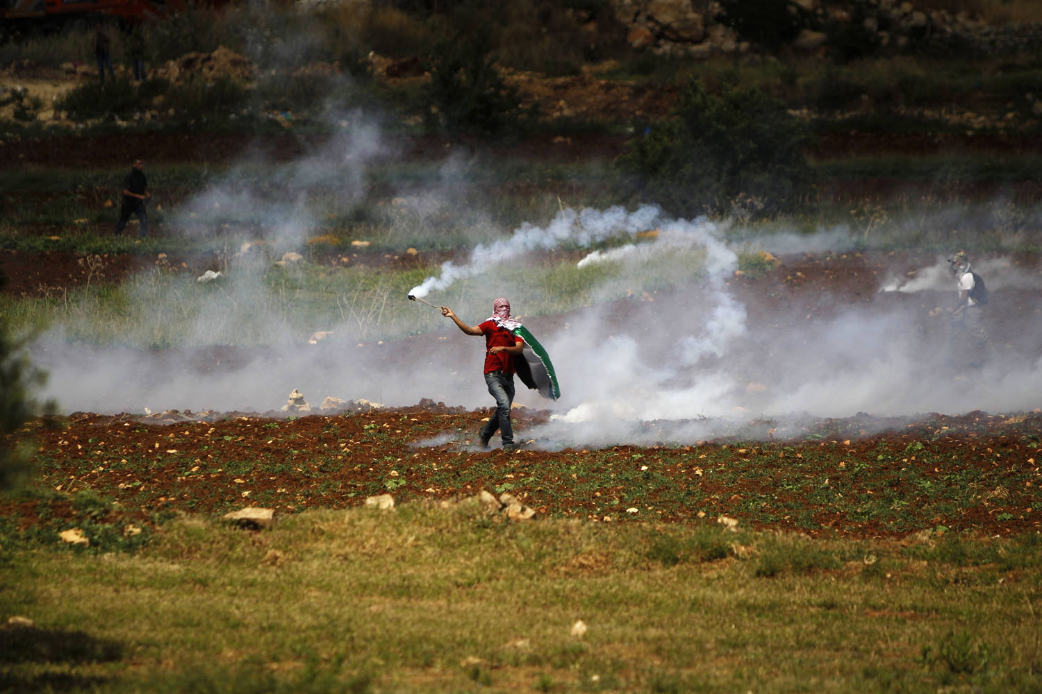 A Palestinian demonstrator returns a tear gas canister towards Israeli  security forces during clashes to mark Nakba Day near the West Bank city of Ramallah