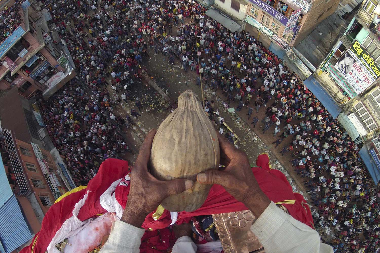 Chakala Dangol, 75, holds a coconut on his hand before throwing it towards the devotees from the top of the chariot of Rato during the chariot festival in Lalitpur