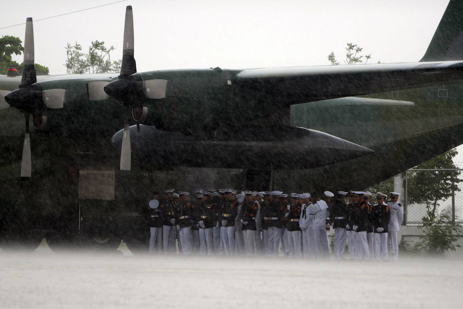 May 26, 2013. Armed Forces of the Philippines (AFP) soldiers take cover from the rain under a C-130 military aircraft while waiting for the arrival of seven coffins of dead soldiers at the Villamor Airbase in Manila.
