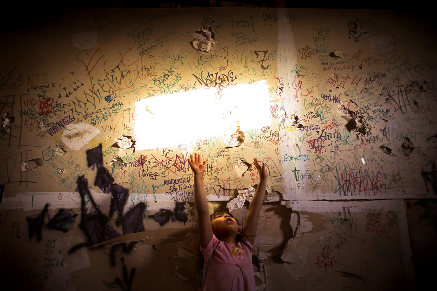 A young girl plays in a basement with graffiti covered walls, Manderson, SD.
