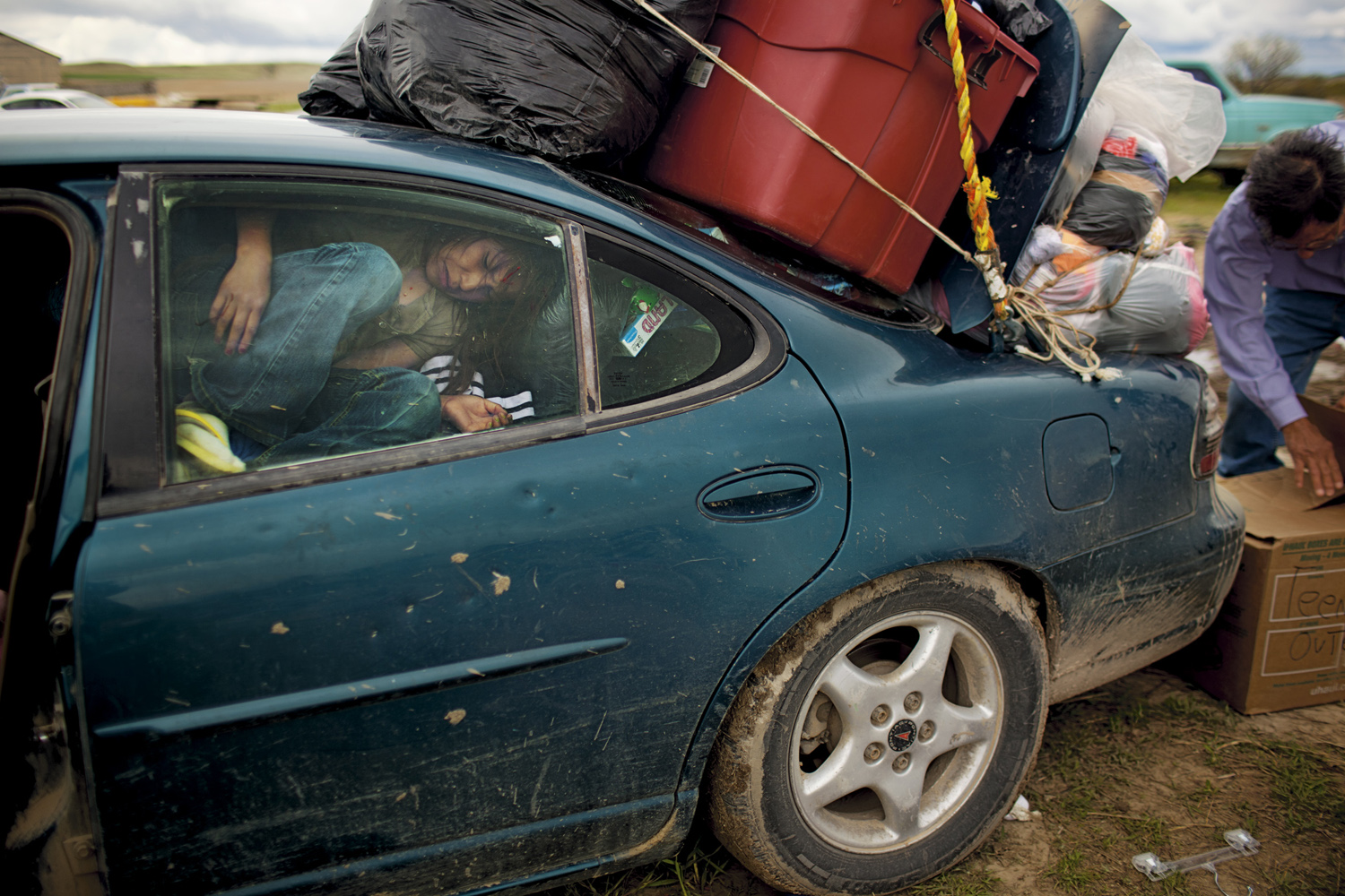 A passenger barely has room for the journey home as a car is loaded with used clothing donated by a Colorado-based Native American charity. Contrary to popular myth, Native Americans do not automatically receive a monthly federal check and are not exempt from taxes. The Oglala Lakota and other Sioux tribes have refused a monetary settlement for the U.S.'s illegal seizure of the Black Hills, their spiritual home.