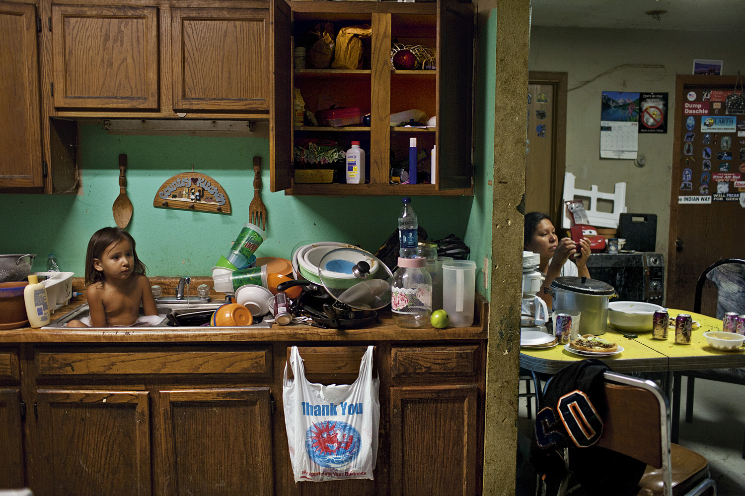 Three-year-old C. J. Shot bathes among dishes. The Oglala concept of tiospaye, the unity of the extended family, means that homes are often overcrowded, especially with the severe housing shortage on the reservation. In 2008, when this photograph was made, 22 people lived in the three-bedroom house.  These houses aren't who we are,  says Oglala activist Alex White Plume.