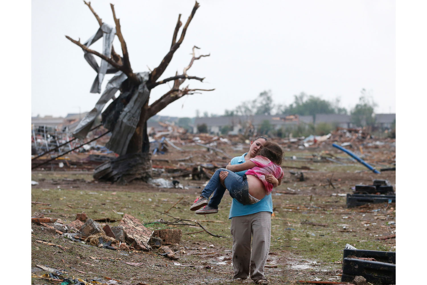 May 20, 2013. A woman carries a child through a field near the collapsed Plaza Towers Elementary School in Moore, Oklahoma. A tornado as much as a mile wide with winds up to 200 mph roared through the Oklahoma City suburbs Monday, flattening entire neighborhoods, setting buildings on fire and landing a direct blow on an elementary school.
