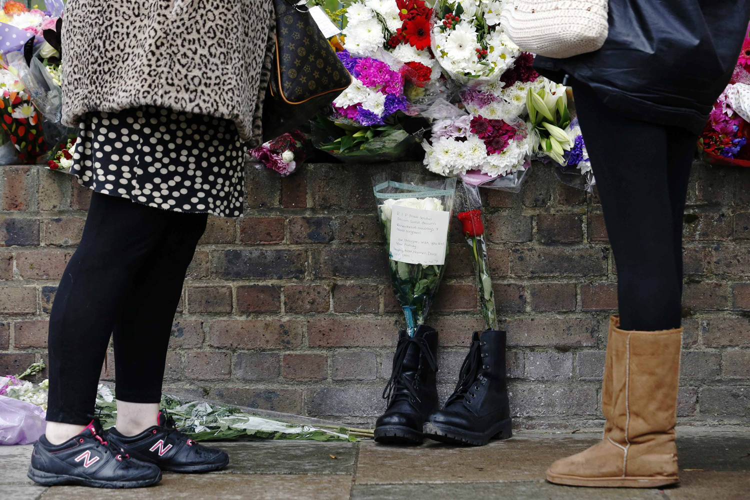 People stand near a pair of army boots and floral tributes for Drummer Lee Rigby near the scene of his killing in Woolwich