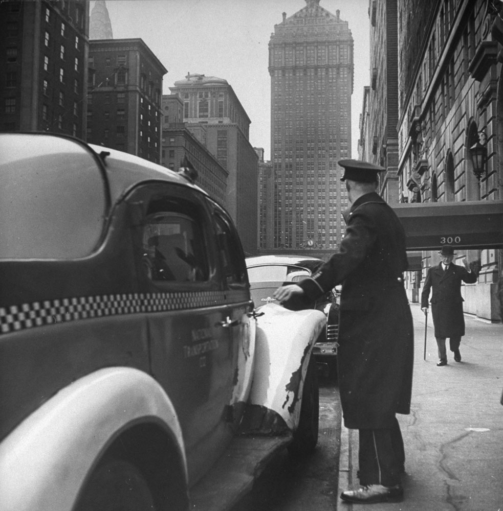 A New York City doorman flags down a taxi for one of the residents of his building, 1944.