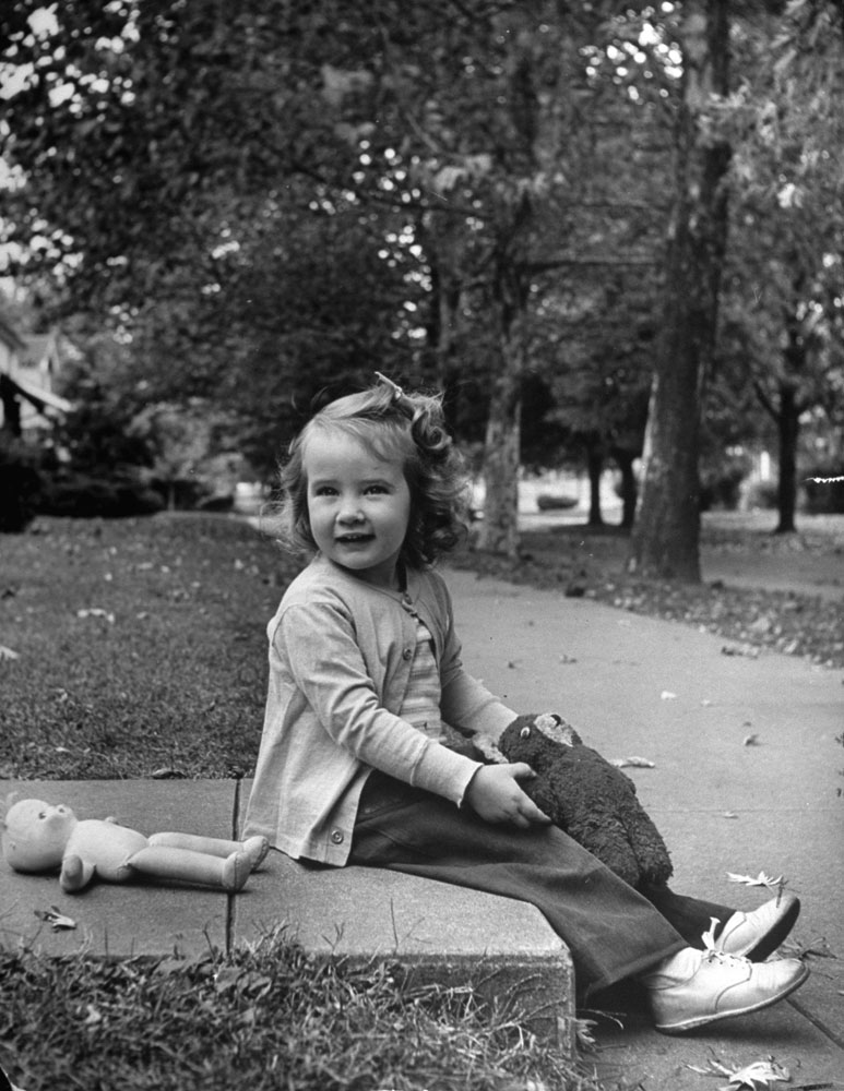 Little girl and her toys on sidewalk, 1948.