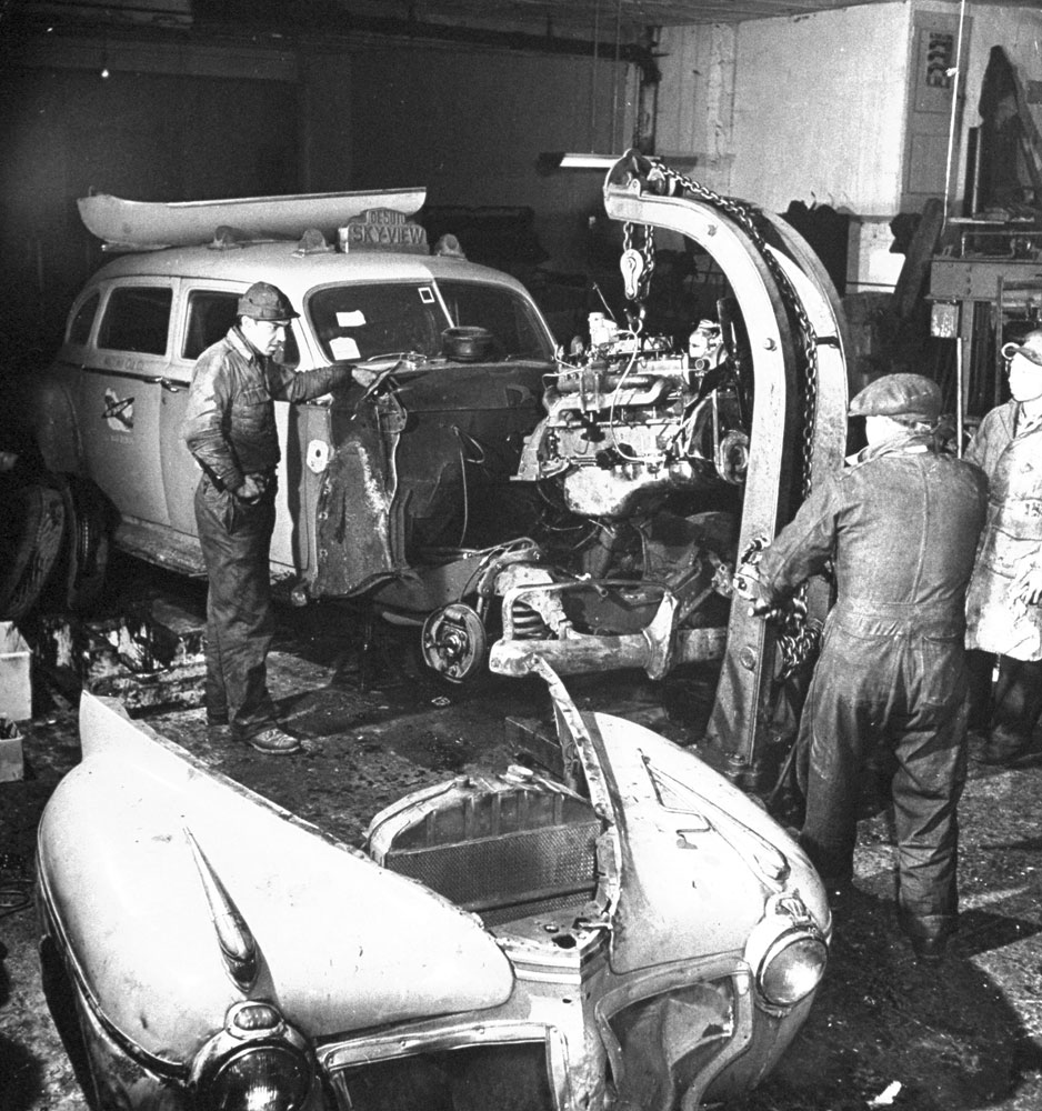 Mechanics use a hoist to drop in the motor of a taxicab under repair at cab company's maintenance garage, NYC, 1944.