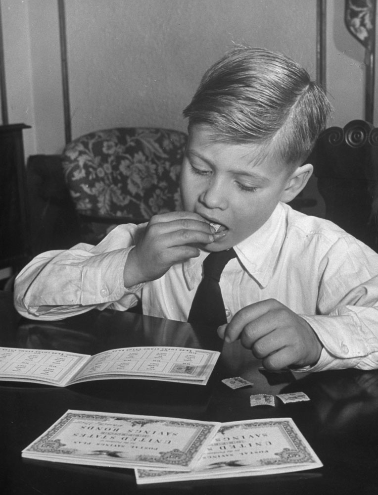 Seven-year-old Billy Mott licks postal stamps in to his Savings Bond book, 1948.