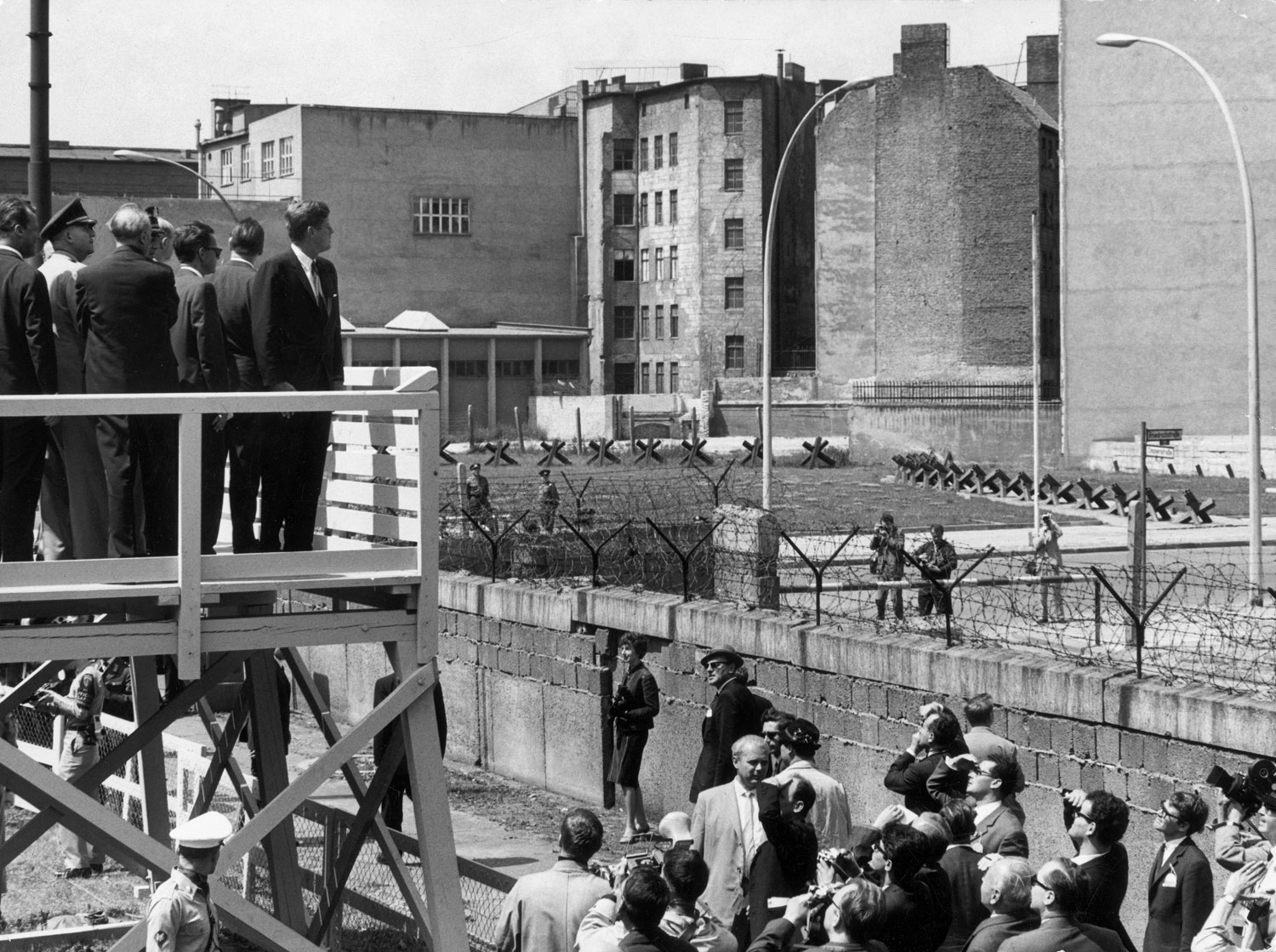 From a viewing stand, President John F. Kennedy gazes over the Berlin Wall into East Germany, June 1963.