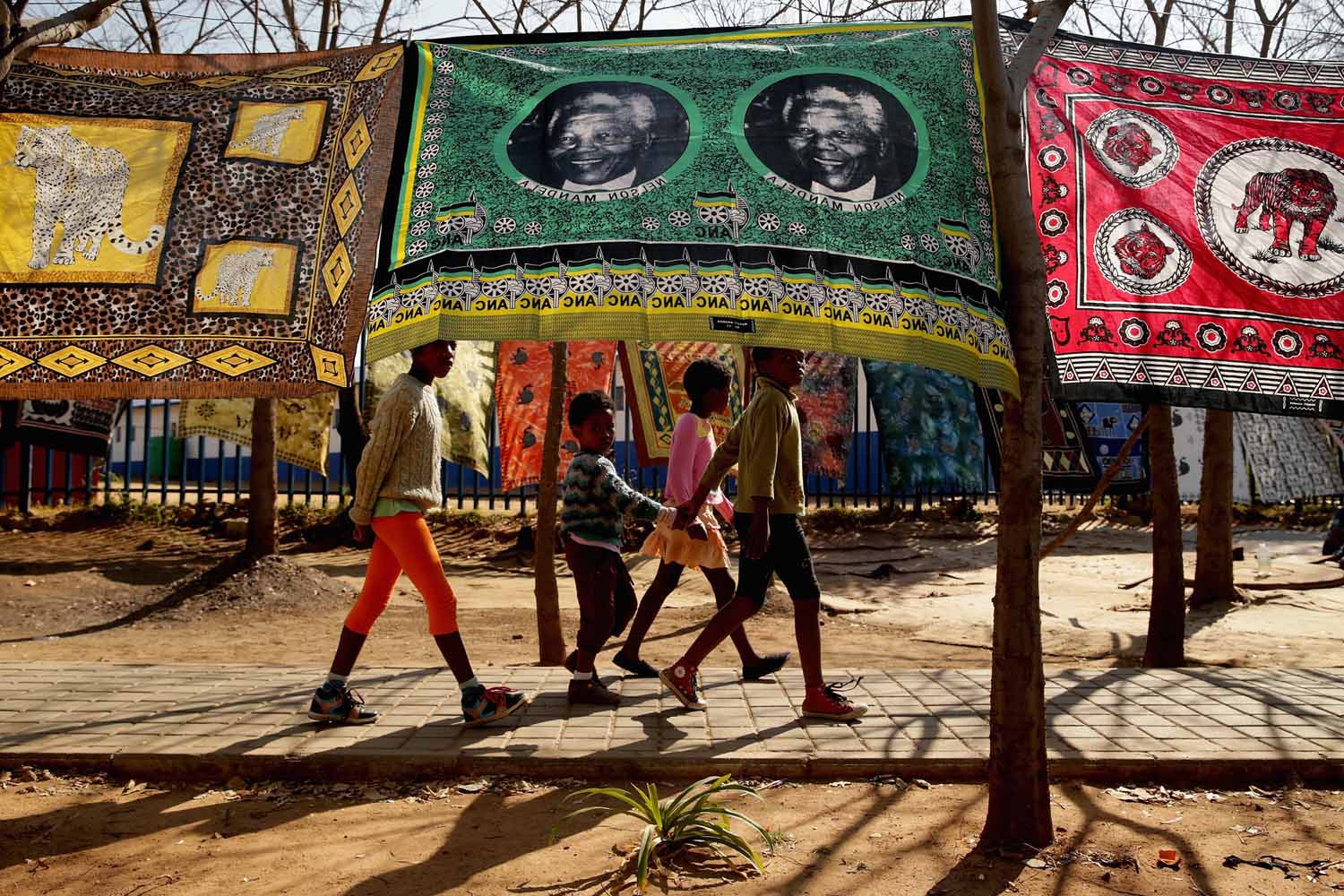 June 24, 2013. Children walk past souvenir flags picturing former South African President Nelson Mandela being sold across from the Hector Pieterson Memorial and Museum in Soweto Township in Johannesburg, South Africa.