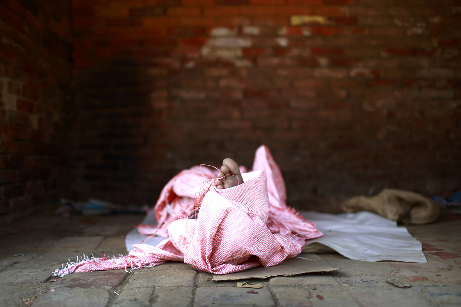 Toe of a street child pokes out from a sack as he sleeps along the streets of Lalitpur