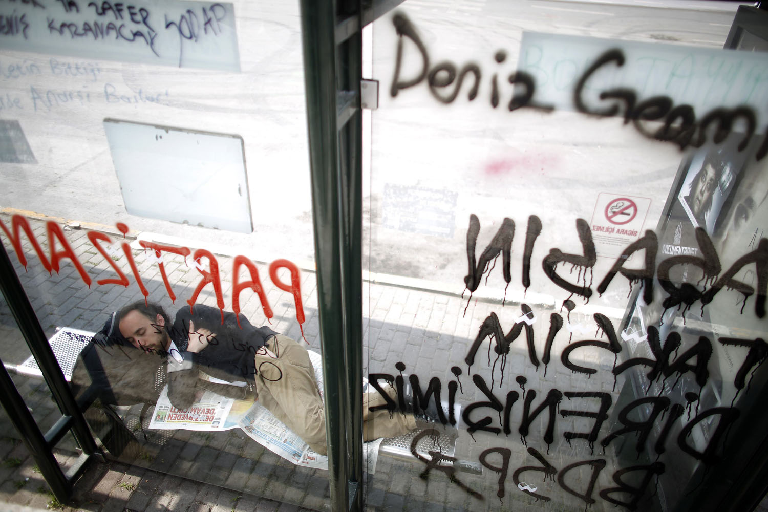 A protester sleeps at a bus stop sprayed with graffiti at Taksim Square in Istanbul