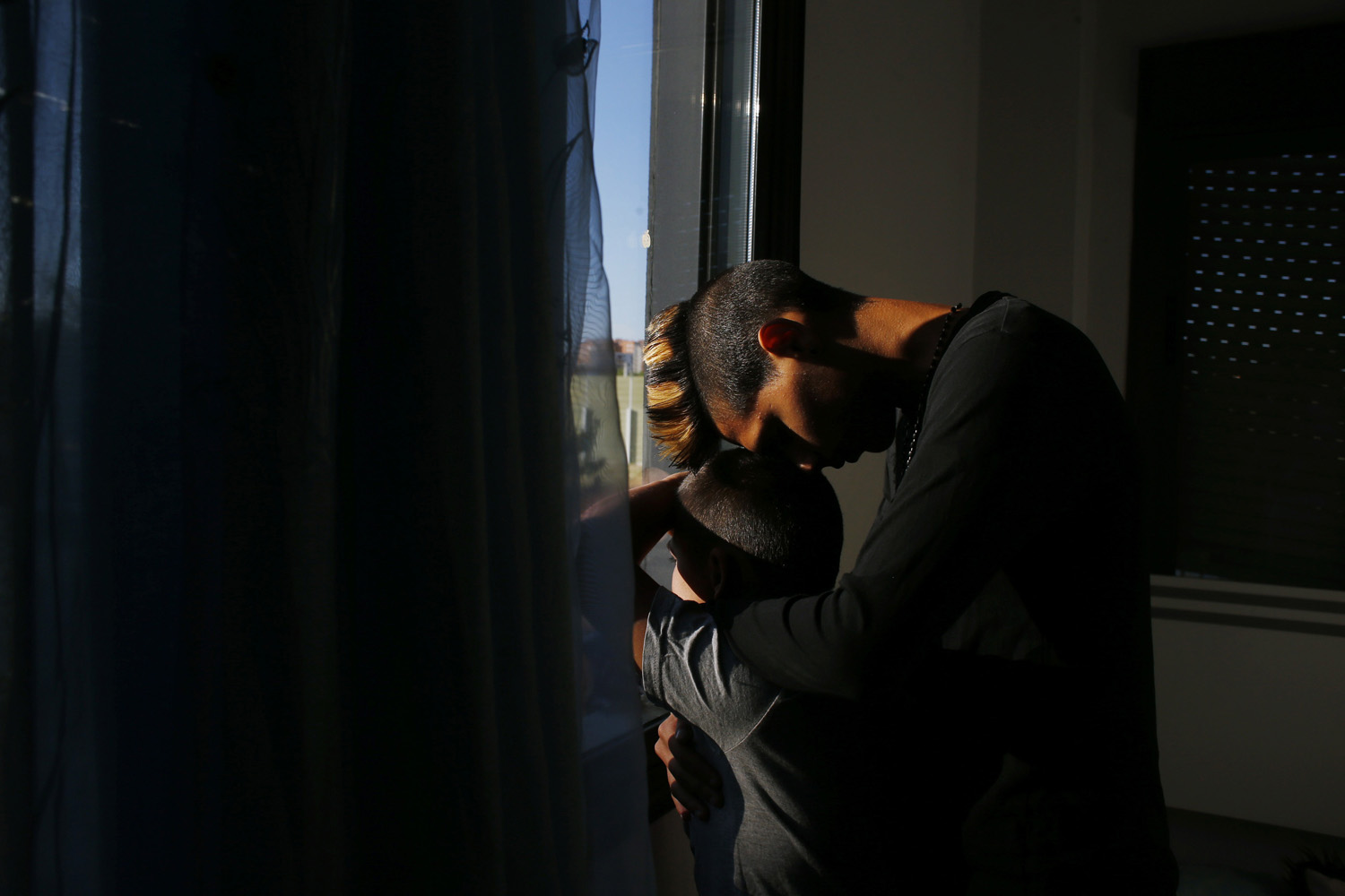 A boy leans on his younger brother as they look out of their window at police officers waiting to carry out their eviction in Madrid