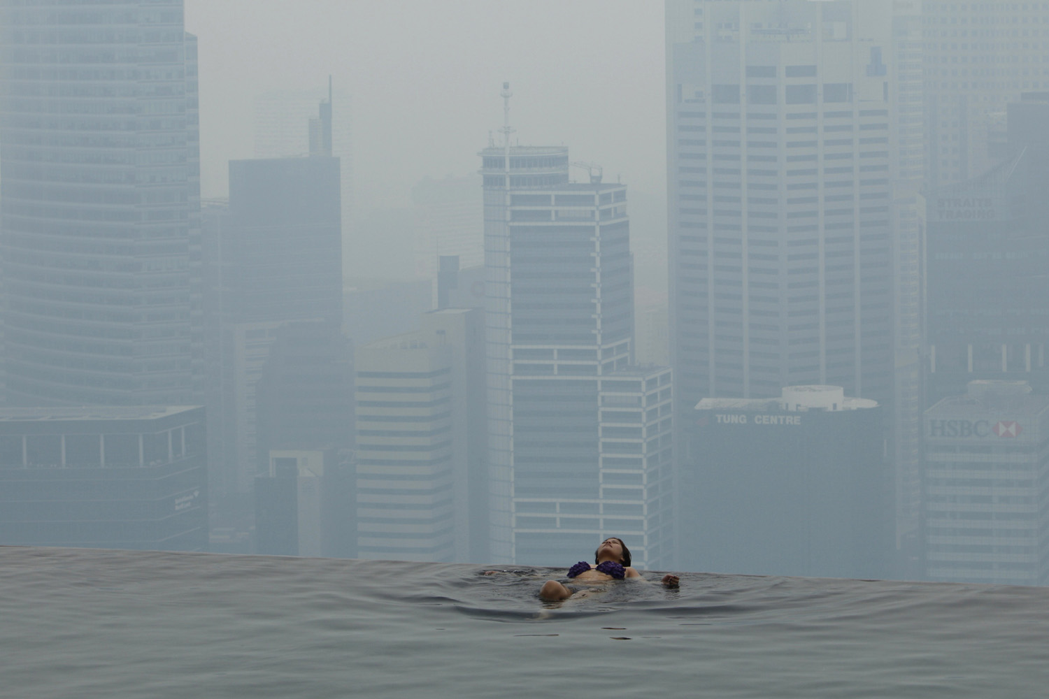 Hotel guest rests in the pool of the Marina Bay Sands Skypark in front of the hazy skyline of Singapore