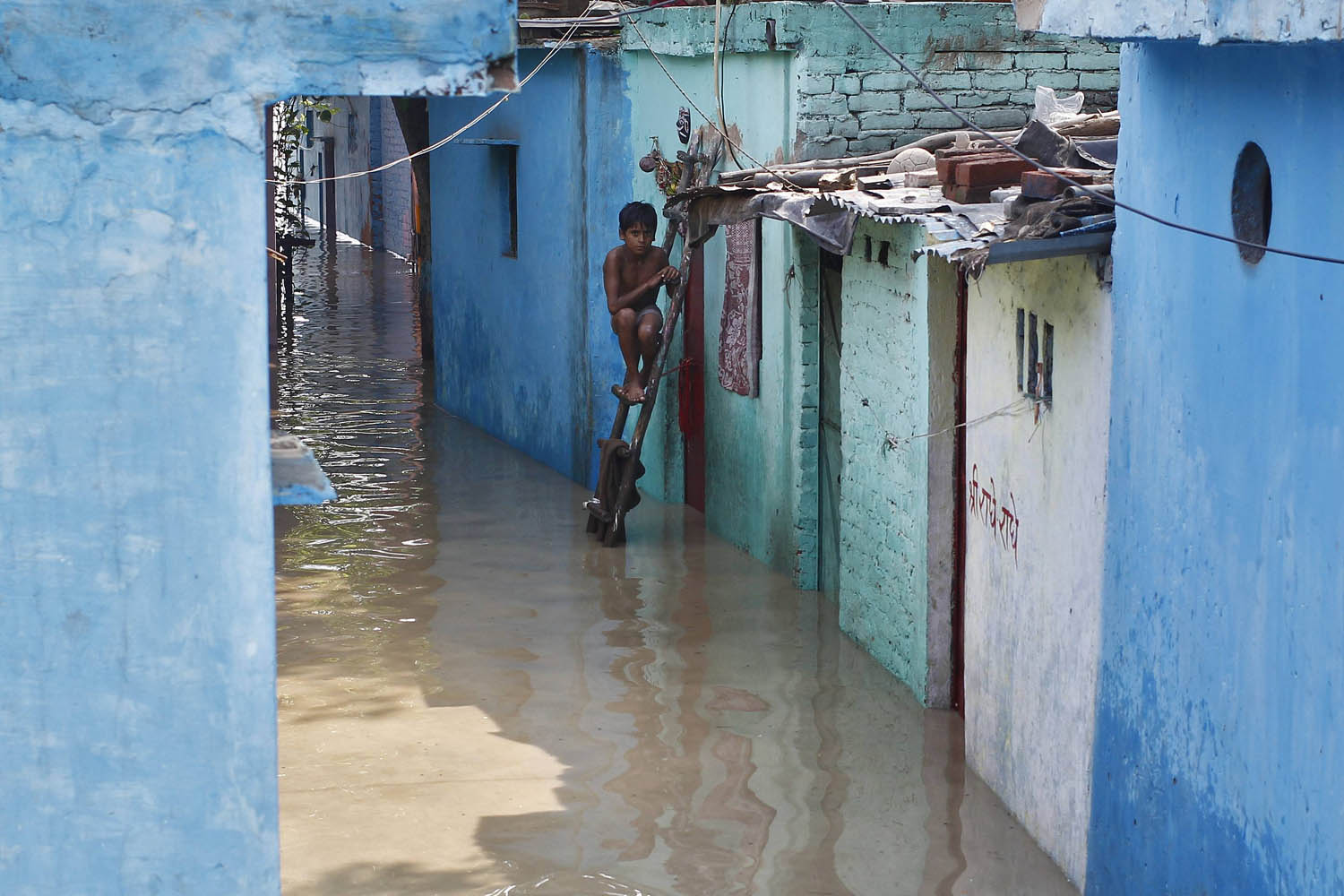A boy sits on a ladder next to his flooded house with the rising water level of river Yamuna after heavy monsoon rains in New Delhi