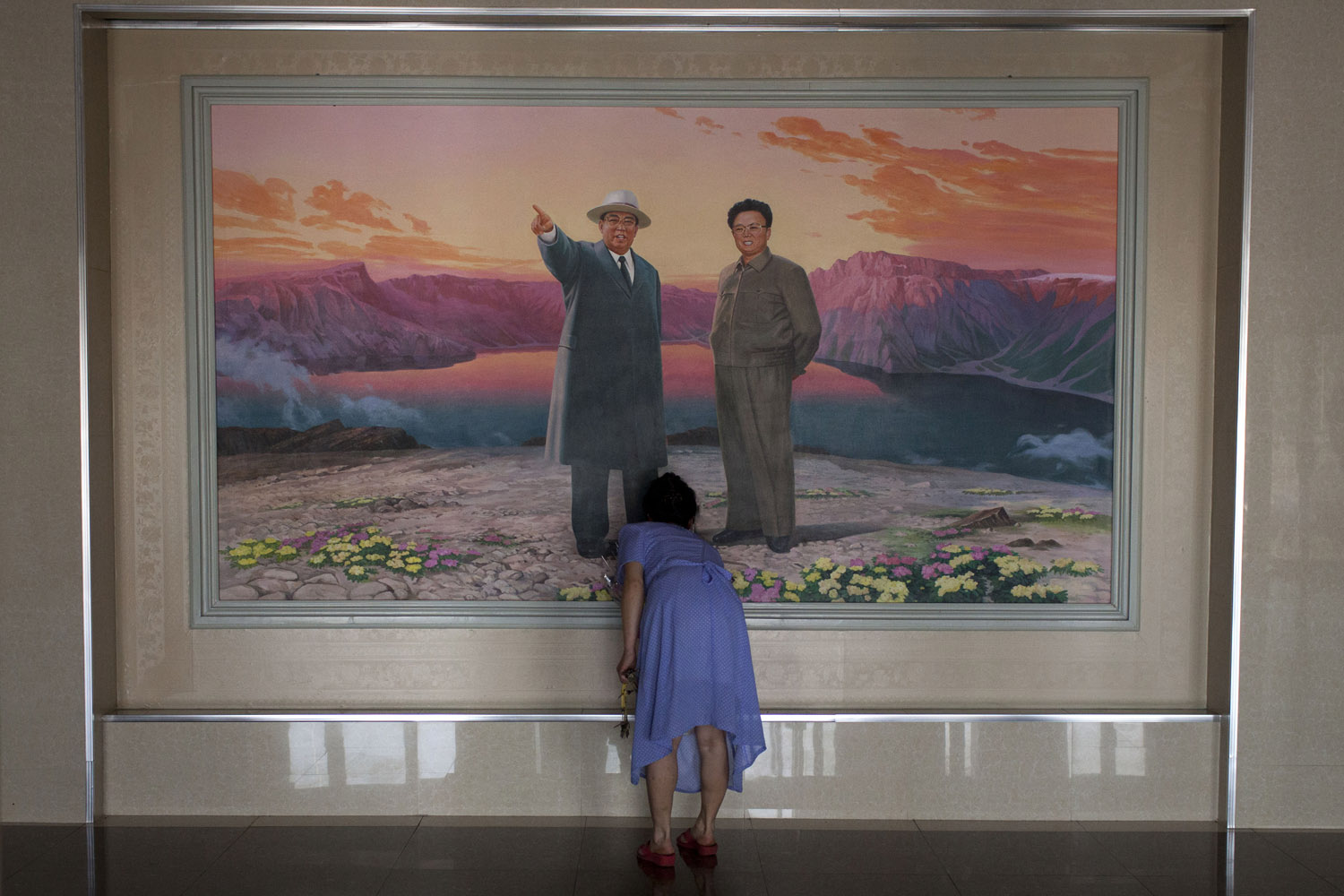 June 21, 2013. A woman arranges flowers in front of a painting depicting the late leaders Kim Il Sung, left, and Kim Jong Il at the lobby of a hotel in Haeju city, South Hwanghae Province, North Korea.