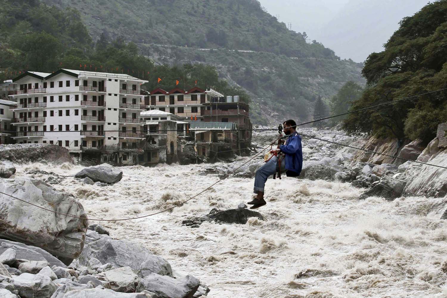 June 23, 2013. An Indian man crosses over a swollen river with the help of a rope in Govindghat, India.