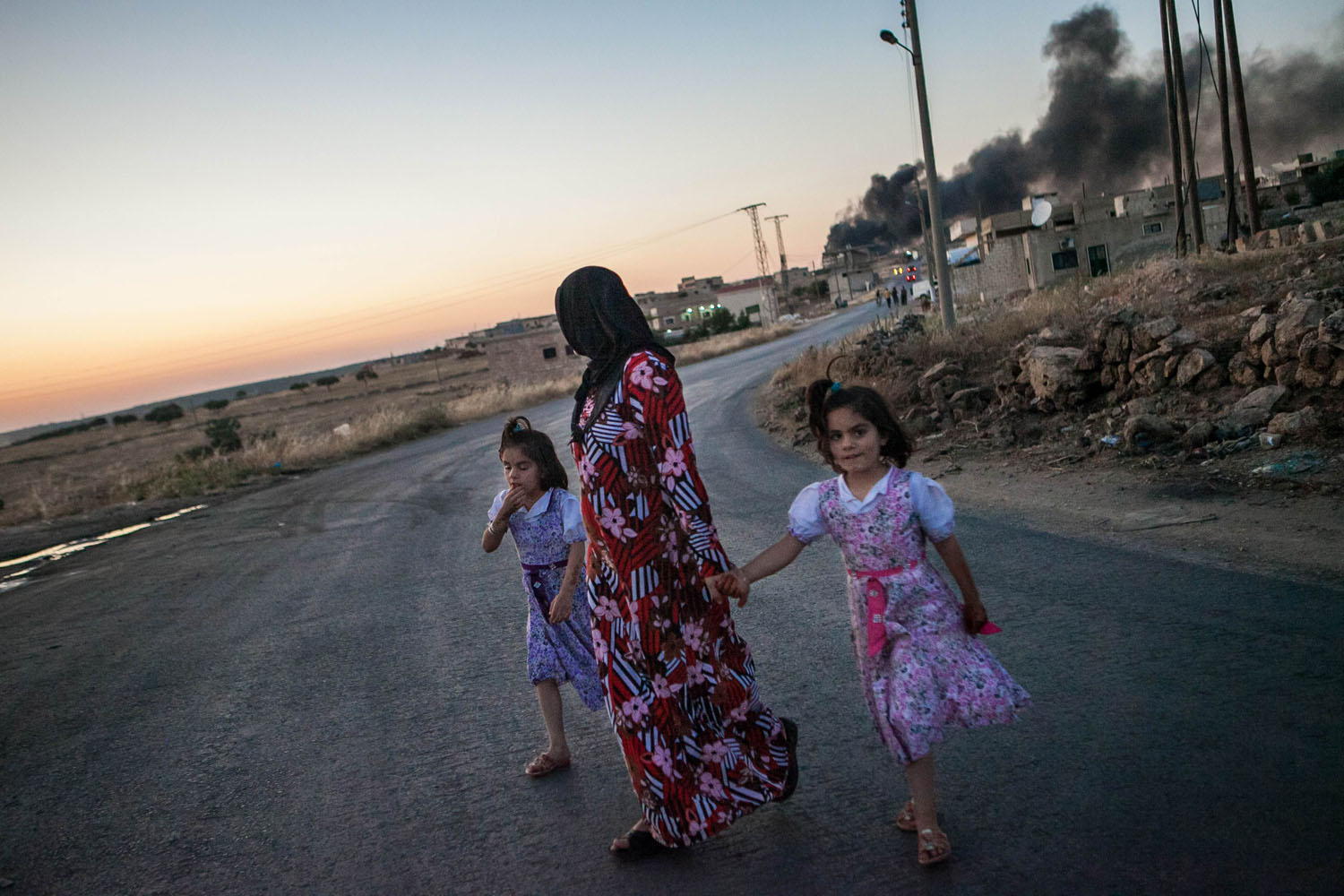 June 24, 2013. Syrian girls walk with their mother as she turns to look at smoke billowing from three mortar shells dropped on the town of Al-Bara in the northwestern province of Idlib.