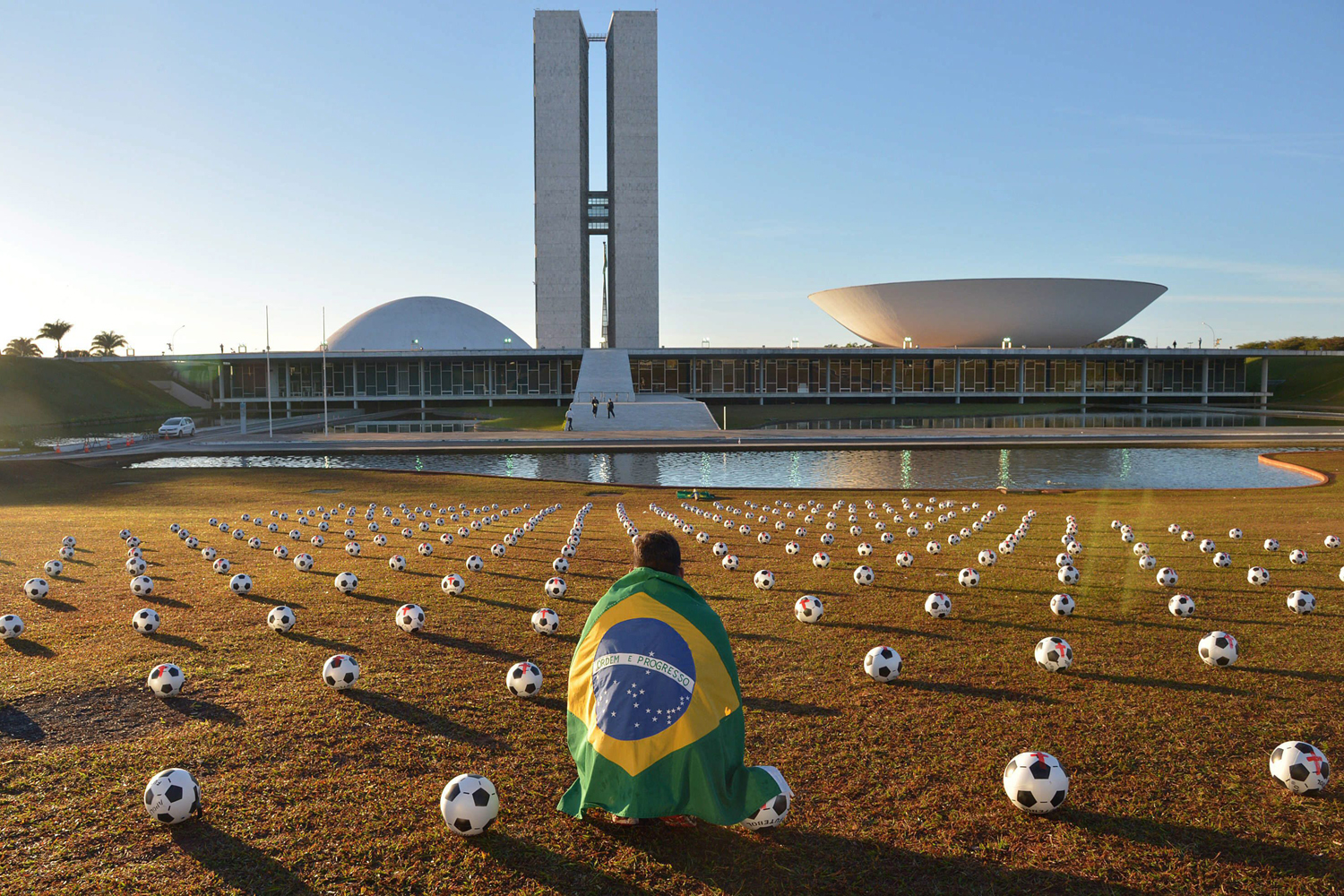 June 26, 2013. A man covered with a Brazilian flag sits amidst the Congress garden where hundred of soccer balls have been set down in protest in Brasilia, Brazil.