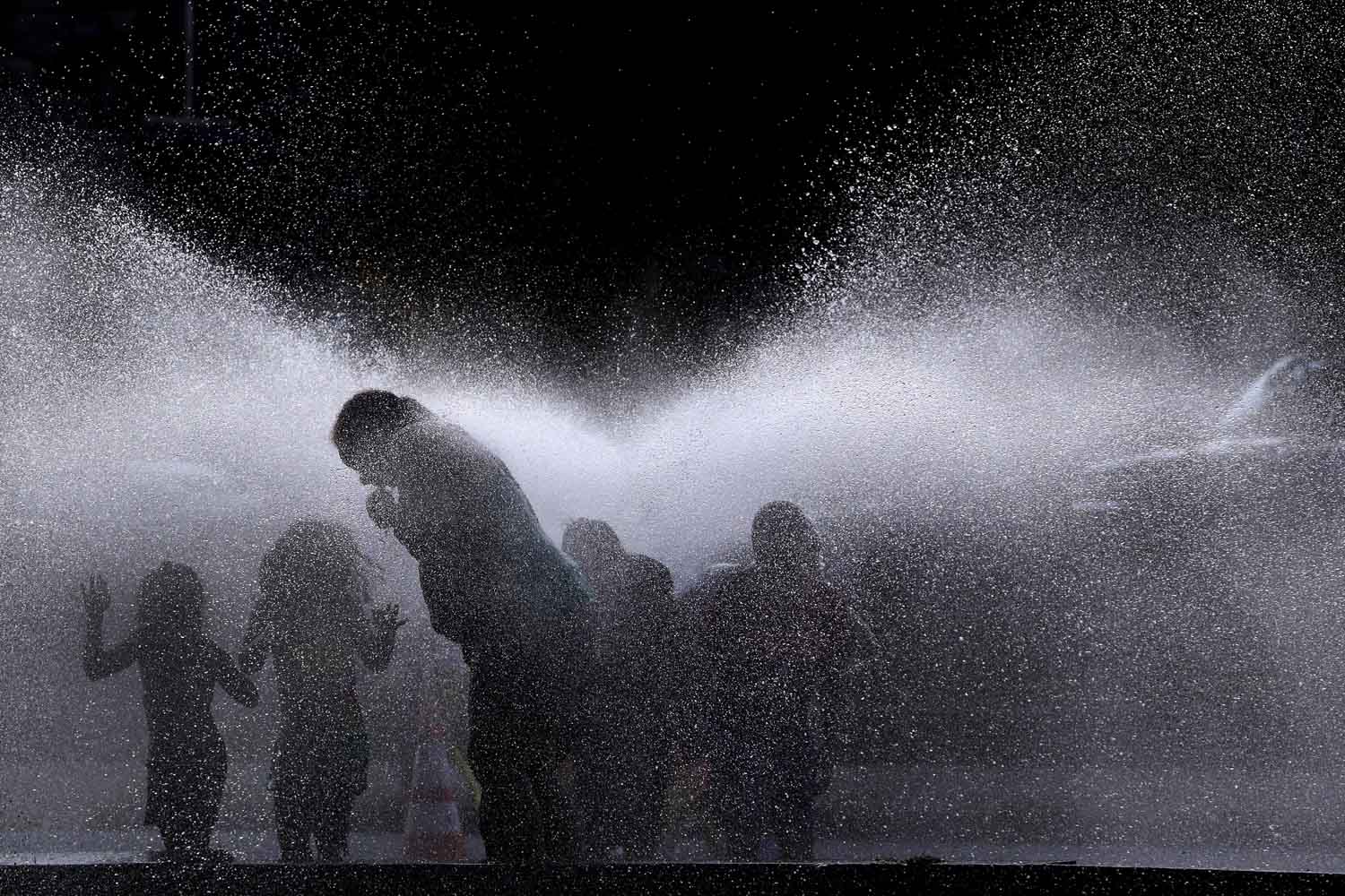 July 16, 2013. People cool off in the spray of an open hydrant on a hot evening in Lawrence, Mass.