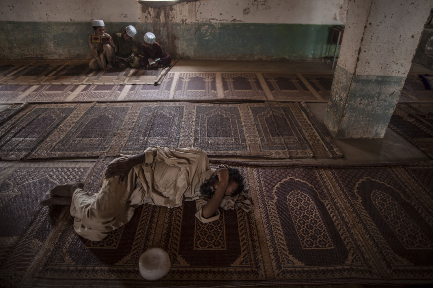 July 17, 2013. An Afghan refugee sleeps on the floor of a mosque, while children read verses of the Quran, during the holy fasting month of Ramadan, on the outskirts of Islamabad, Pakistan.