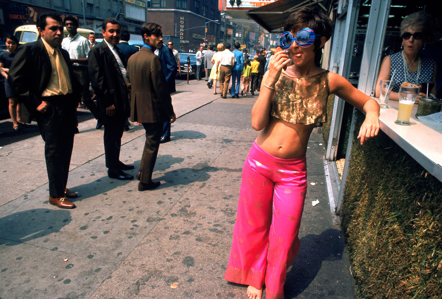 Men ogle a young woman wearing pink pants and a gold top, New York City, summer 1969.