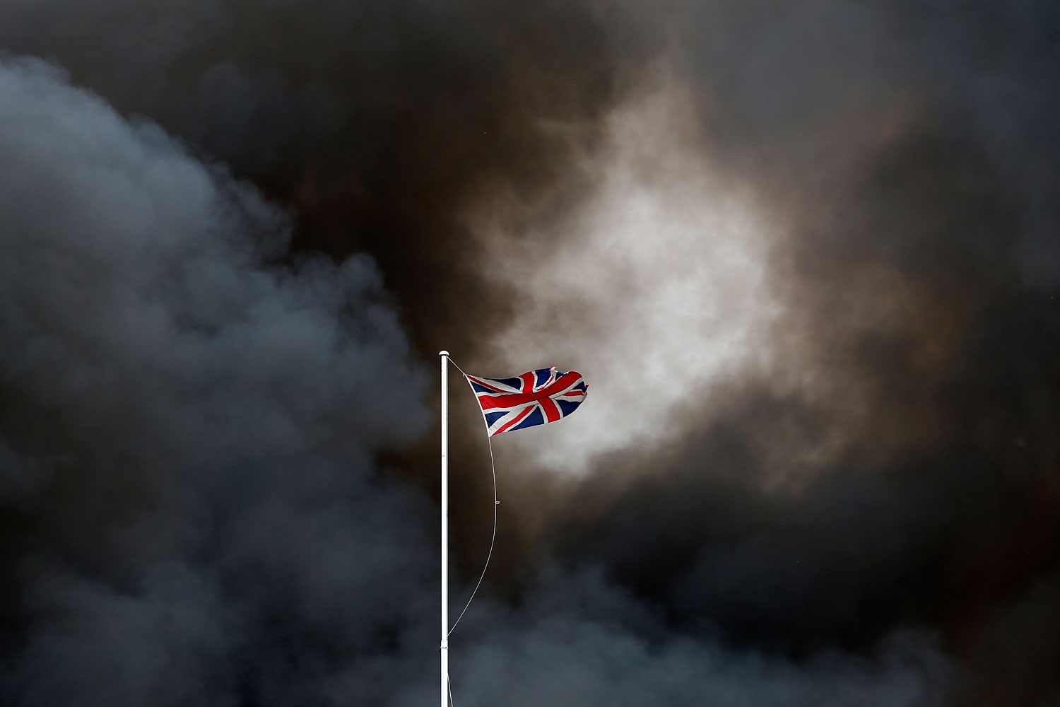 July 1, 2013. Smoke rises behind the Union Flag from a fire at a recycling plant in Smethwick, central England. Firefighters are tackling the blaze involving 100,000 tons of plastic recycling material.