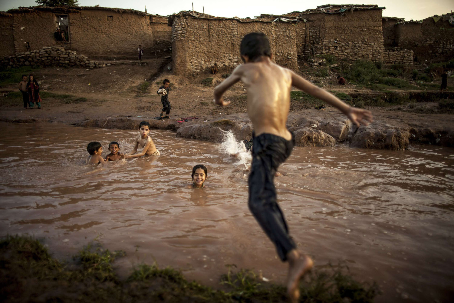 A boy, whose his family fled military operations in the western tribal area, jumps into a stream in a slum on the outskirts of Islamabad