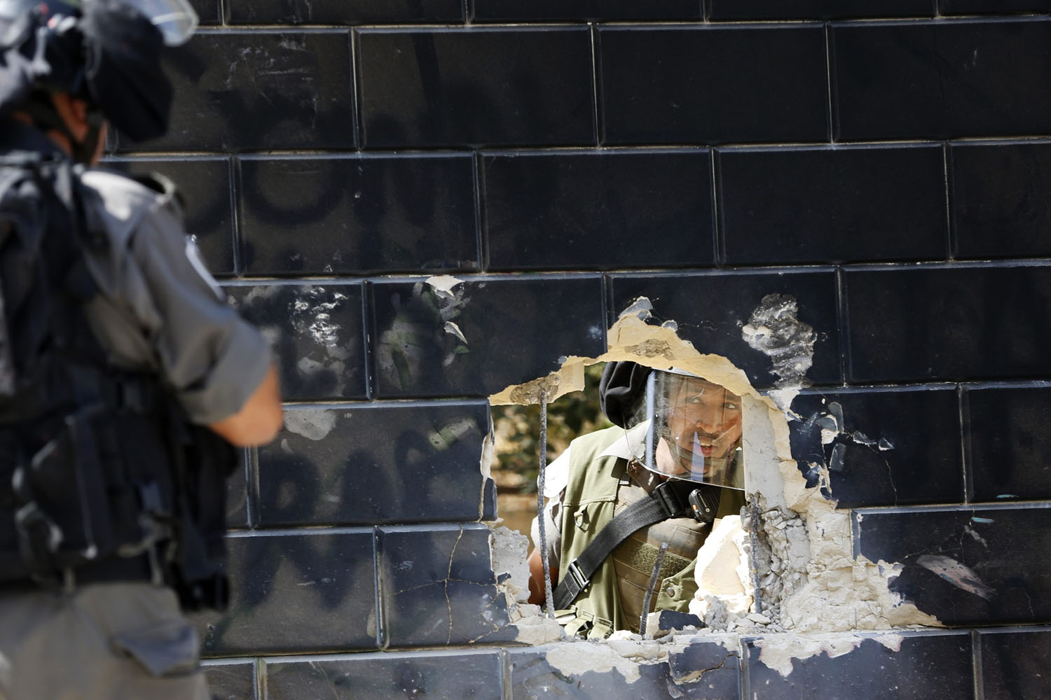 An Israeli border policeman looks at his colleague through a hole in a section of the controversial Israeli barrier near Jerusalem
