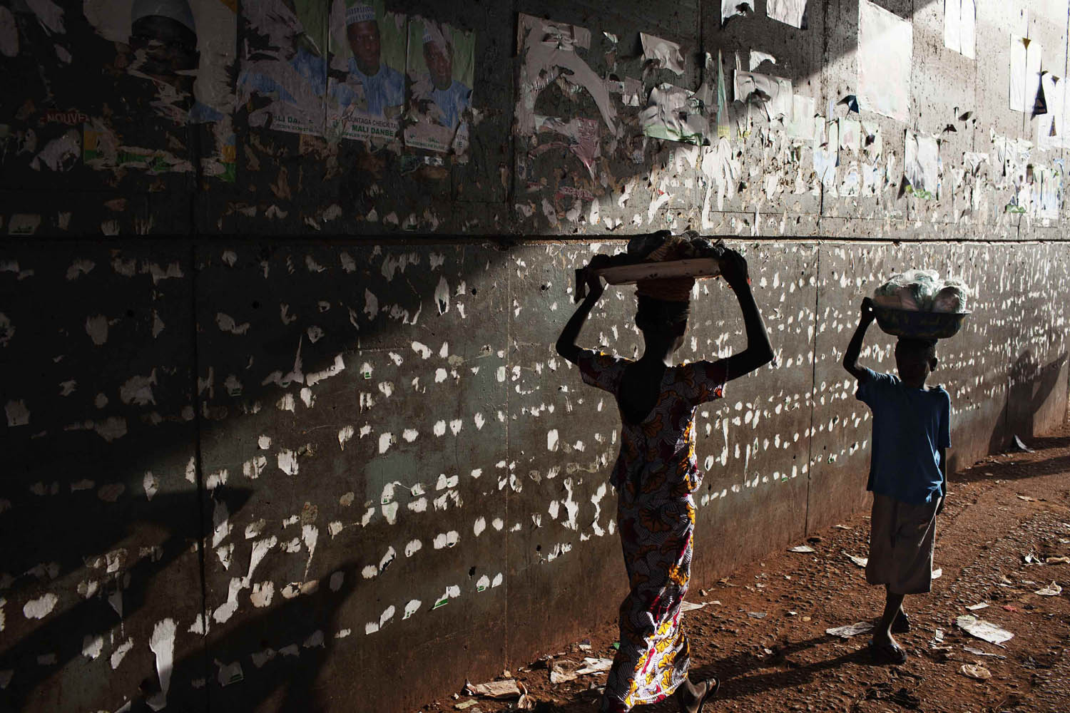 Children walk in front of ripped presidential campaign posters in Bamako