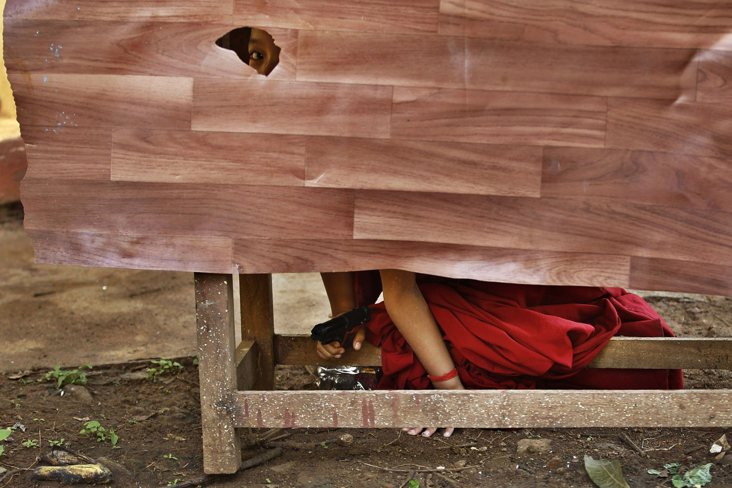 July 15, 2013. A novice Tibetan Buddhist monk peeps through a hole as he hides behind a desk holding a toy gun during a break from their spiritual leader the Dalai Lama's religious sermon outside the Gyudmed Tantric Monastery in Gurupura 132 miles southwest of Bangalore, India.
