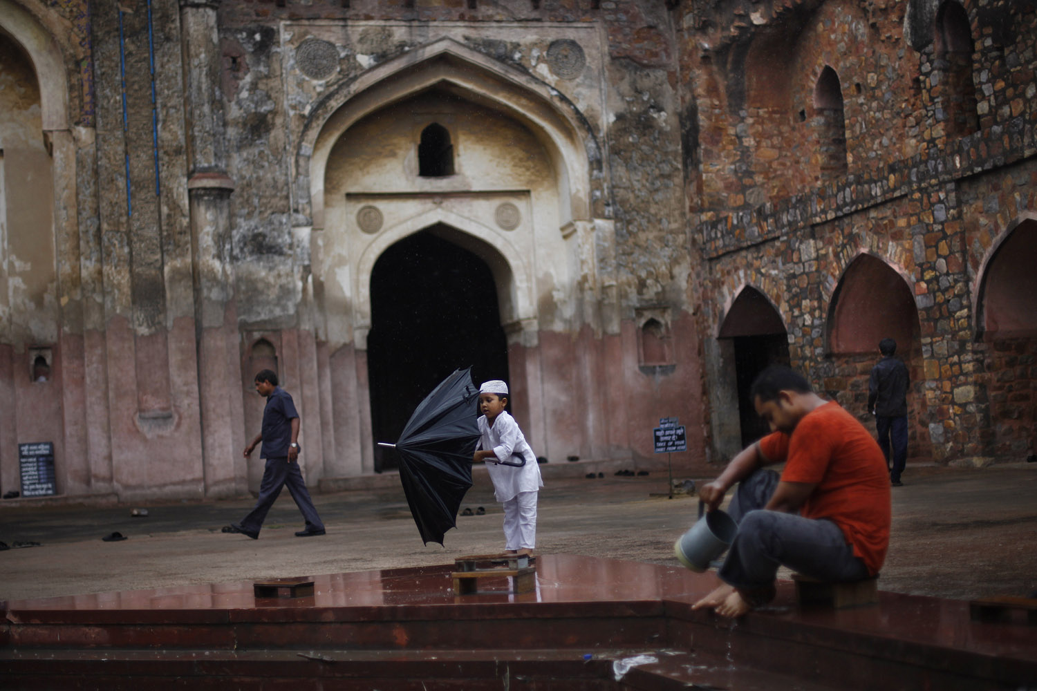 July 12, 2013. A young Indian Muslim boy tries to fold an umbrella on the first Friday of the holy month of Ramadan at an old Mughal era mosque in New Delhi.