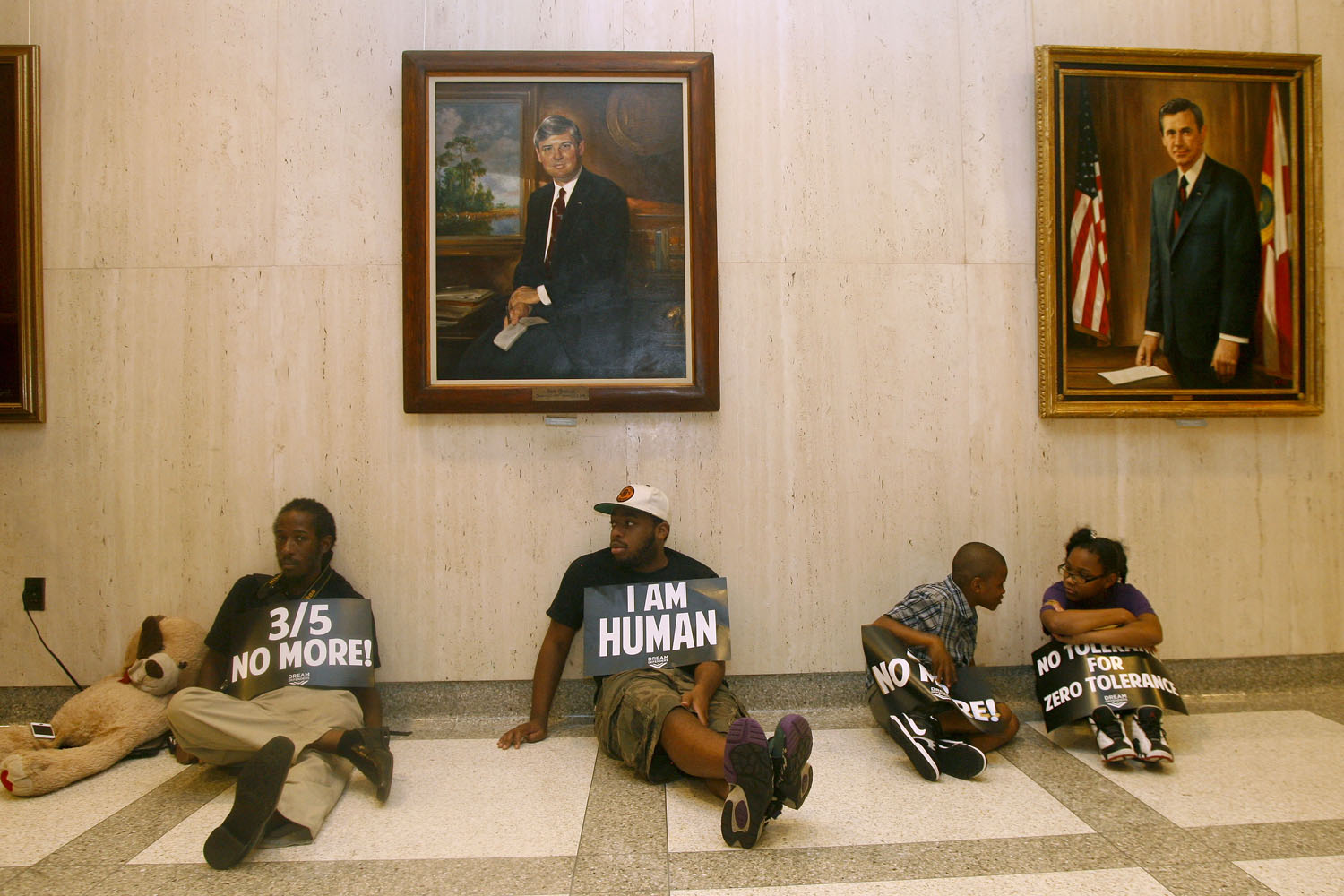 July 17, 2013. Under portraits of former Florida Governors Bob Graham and Reuben Askew, protestors sit on the floor outside Florida Gov. Rick Scott's office at the Capitol in Tallahassee.
