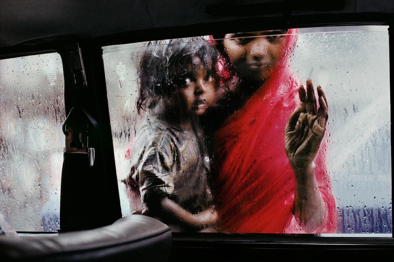 Mother and child looking in through a taxi window, Bombay, India, 1993
                              
                              
                              ‘I was in a taxi waiting at a traffic light during the monsoon, and a woman brought her child up to the car window. I raised my camera, took two frames, the light changed, and off we went – it all happened in about seven or eight seconds. Two months later, I came across these two frames when I was editing the pictures in New York. I was delighted that the picture came out as well as it did. It seemed to symbolize the separation between my world and hers – I’m in this air conditioned bubble, she’s out there in the heat and the rain – and how those two worlds came together for a moment.’