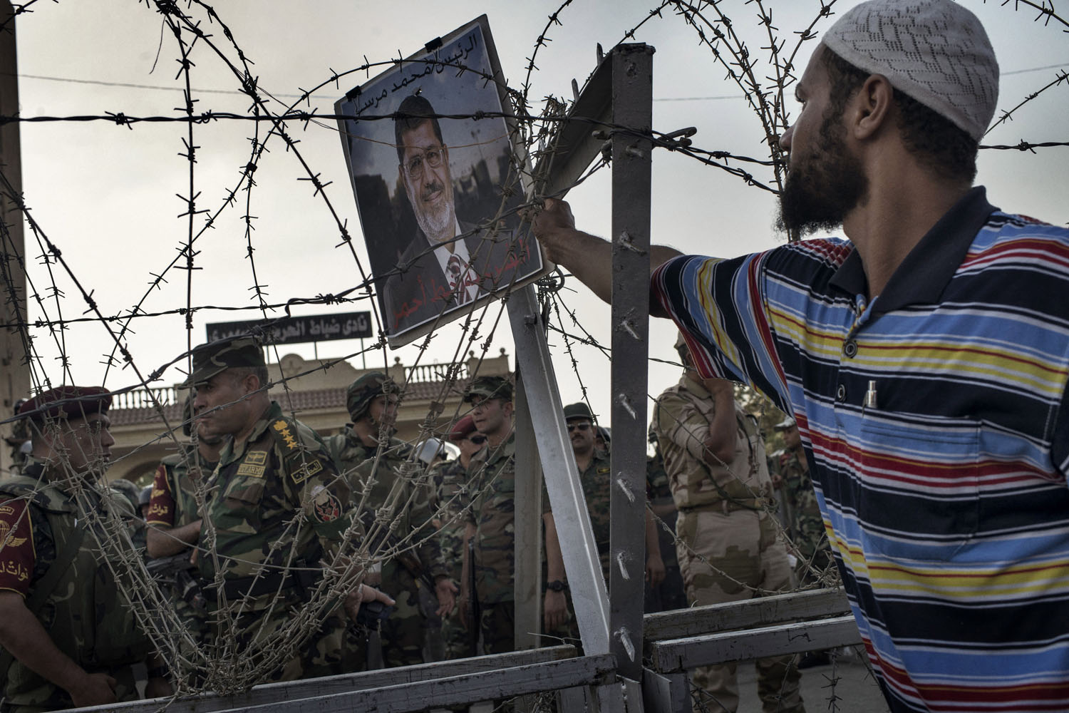 July 5, 2013. A Morsi supporter places a poster of the ousted Egyptian president on barbed wire outside the Cairo headquarters of the Republican Guard.