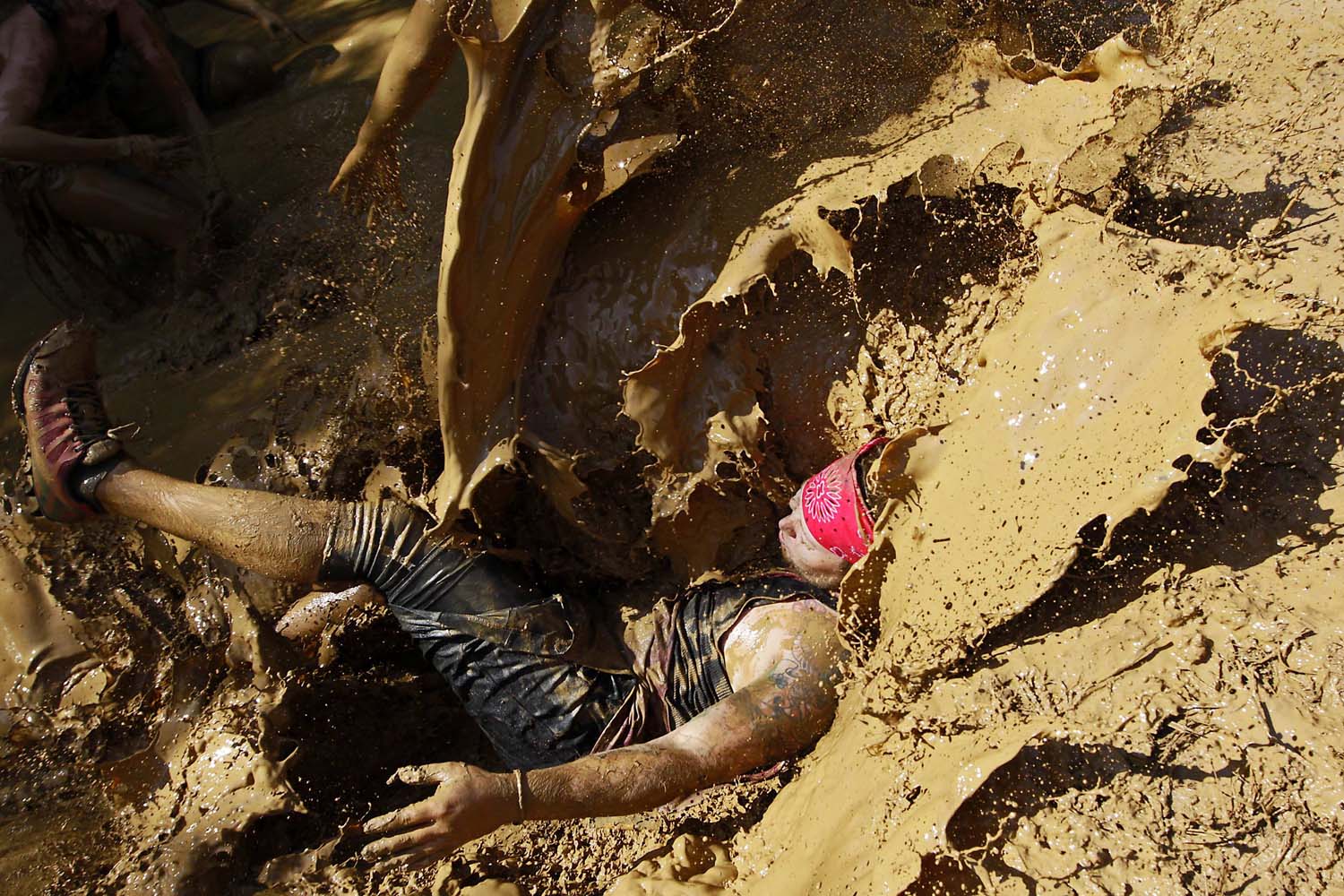 A participant falls into muddy water after getting over a muddy mound during the Warrior Dash obstacle race in Crawfordsville