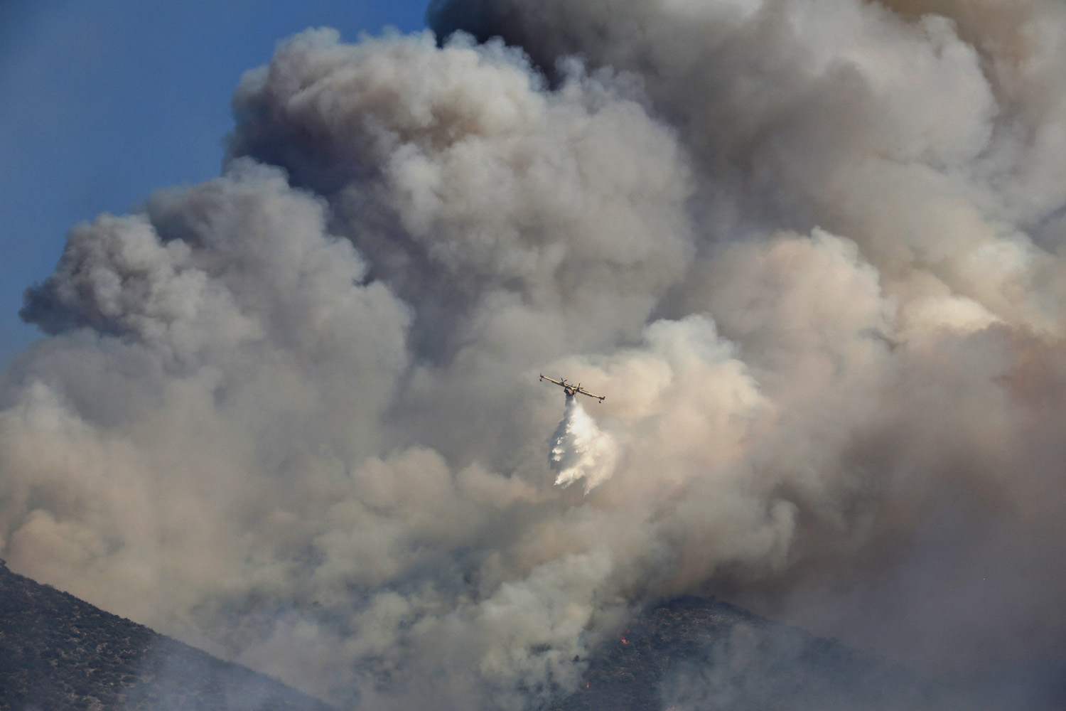 A firefighting airplane drops water over a forest fire at Markopoulo region