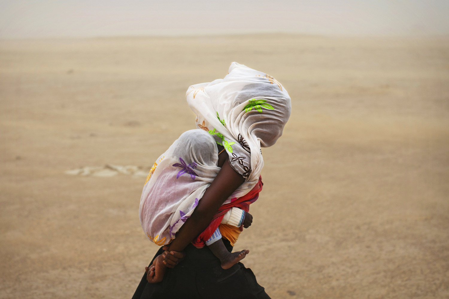 July 29, 2013. A woman carrying her baby and wrapped with a shawl walks through a sandstorm in Timbuktu.