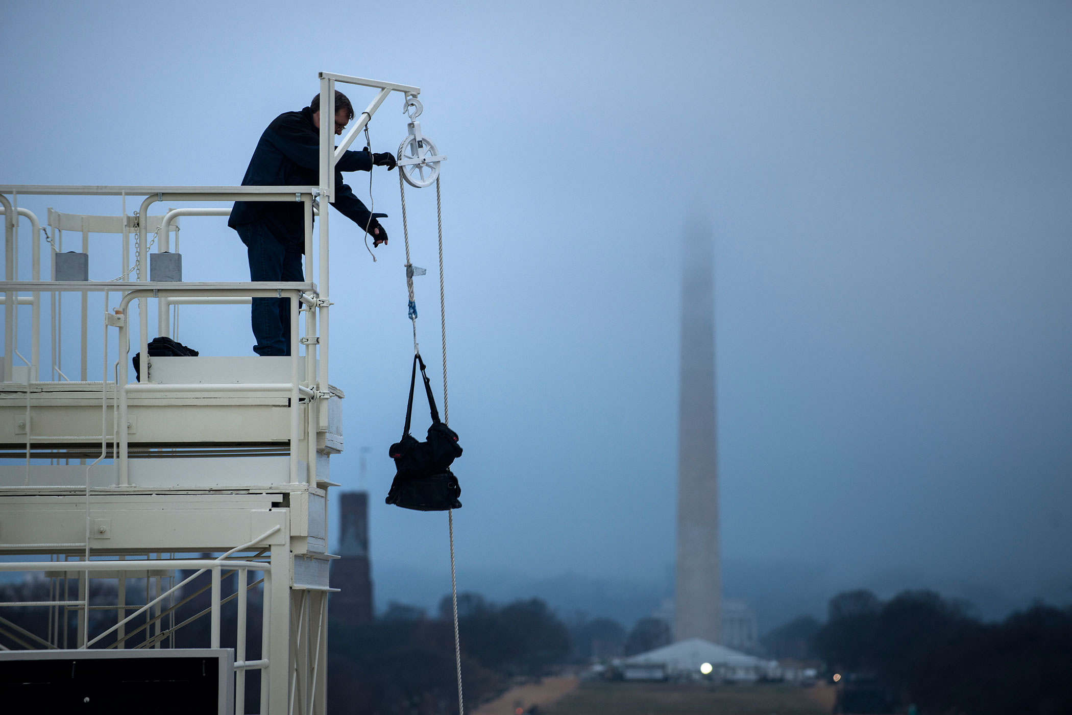 Jan. 13, 2013. A worker uses a pulley to bring a bag to the top of a camera tower before an inauguration rehearsal on Capitol Hill in Washington.