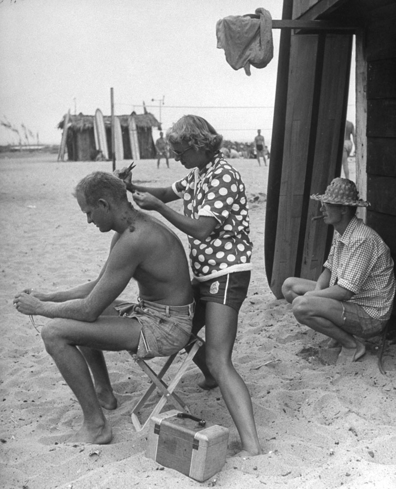Haircutter to all the beach bums is Myra Roche, mother of three children. She helps friend Warren Miller make ends meet by shearing his hair free.