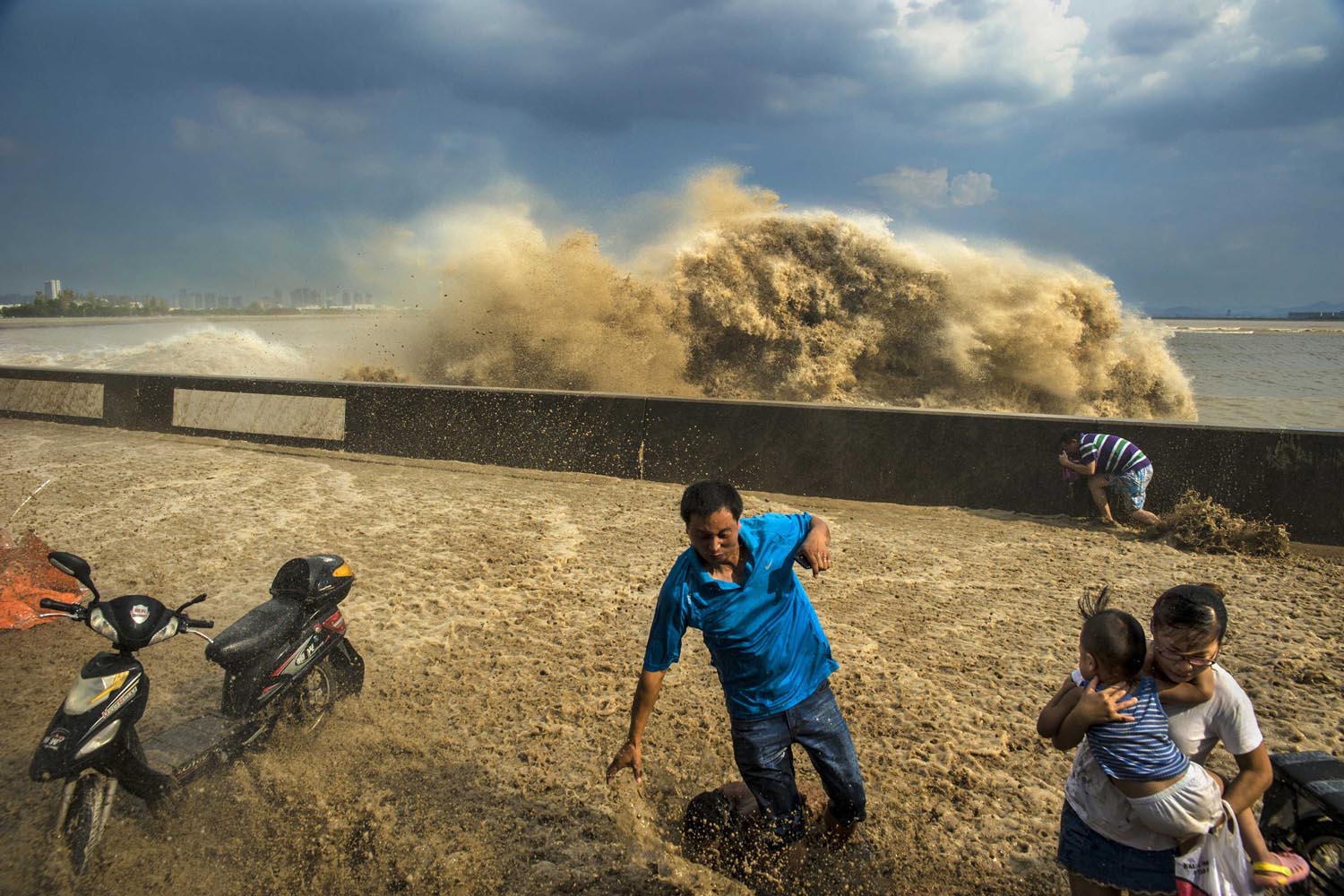 Visitors run away as waves from a tidal bore surge past a barrier on the banks of Qiantang River, in Hangzhou